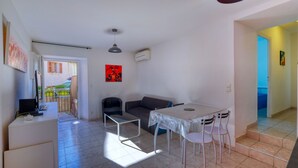 Un espacio habitable compacto con kitchenette, una zona de comedor con mesa y sillas, un sofá y un cuadro en la pared.