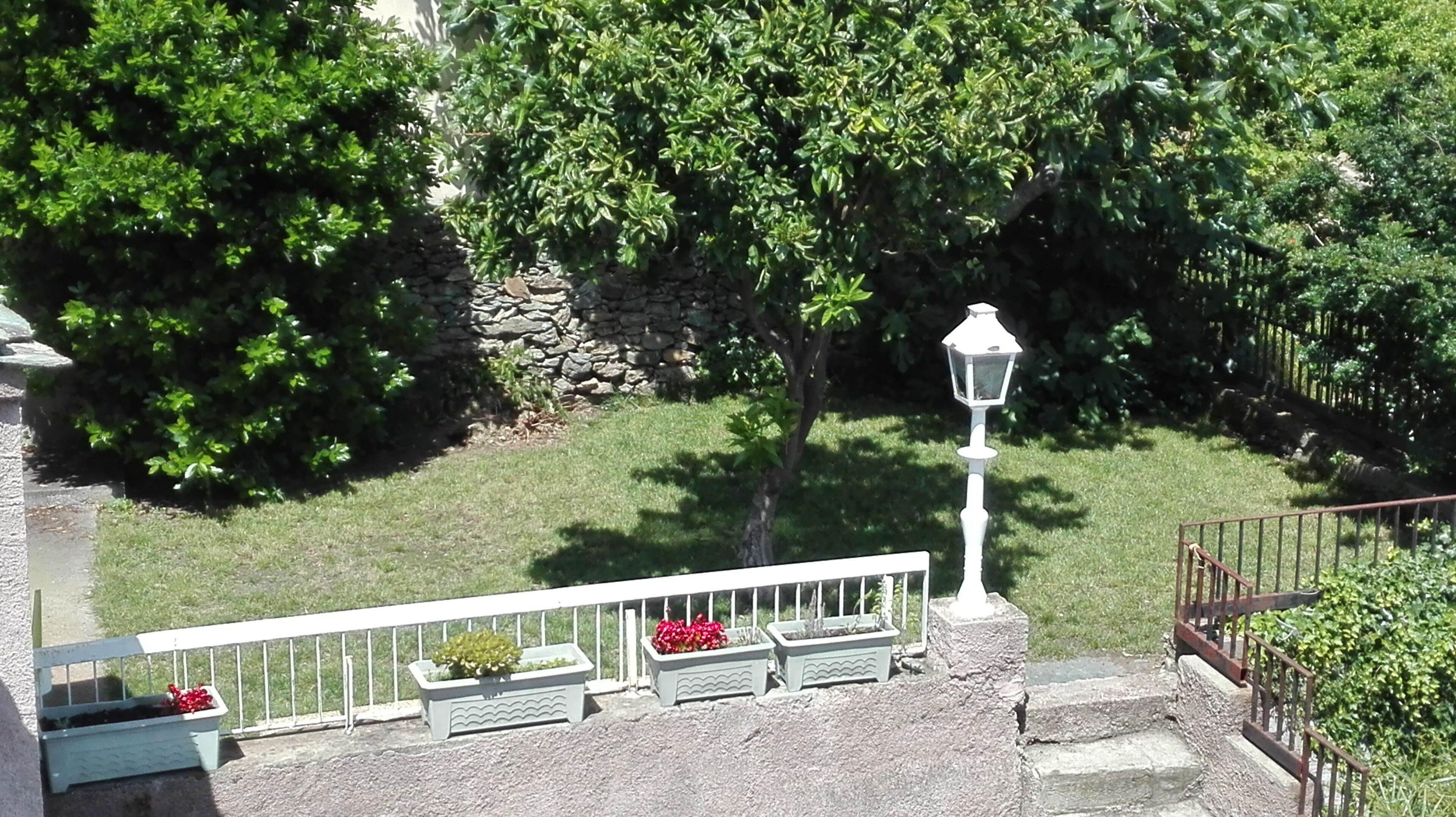 Un mur de pierre avec un petit espace aménagé en jardin, un lampadaire blanc et une rambarde en métal.