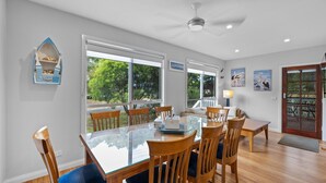A dining area with a glass-top table, wooden chairs, and a view of greenery outside. - Cowes Beach and Boat House (COWES)