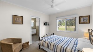 A bedroom with a bed, a chair, a TV, and a window with a view of trees. - Cowes Beach and Boat House (COWES)