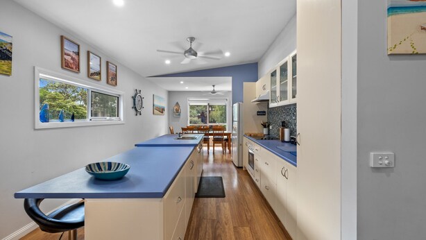 A modern kitchen with a long island, wooden cabinets, and a view to the dining area. - Cowes Beach and Boat House (COWES)