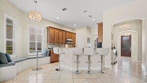 A modern kitchen with a central island, bar stools, and a seating area with a view to the outdoors. - Homestead Beech: Private Pool, Golf, Water Park, Near Disney (Kissimmee)