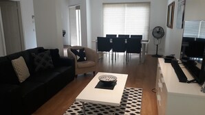 A modern living room with a black sofa, a beige armchair, a white coffee table, and a dining area with a black table and chairs. - Jewel on Jenner in Cowes (COWES)