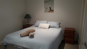 A bedroom with a bed, pillows, a lamp, a painting, and a teddy bear. - Jewel on Jenner in Cowes (COWES)