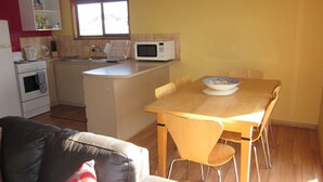 Une cuisine compacte équipée d’un four à micro-ondes, d’un évier et d’une cuisinière. On y trouve une table à manger avec des chaises et un saladier rempli de fruits.