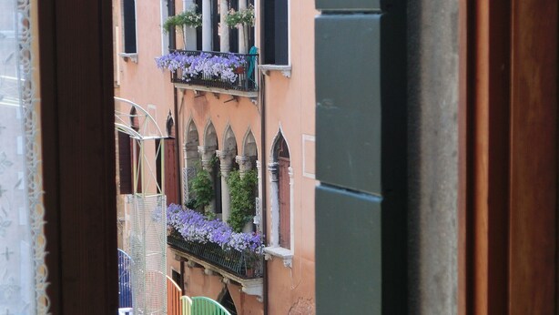 A view from a balcony with a wrought iron railing, a small table, and chairs. In the background, there is a building with arched windows and balconies adorned with flowers. - BEST VIEW AND SUNNY Cà DEL SOL IT027042C2W4RXWZRV (Venezia)