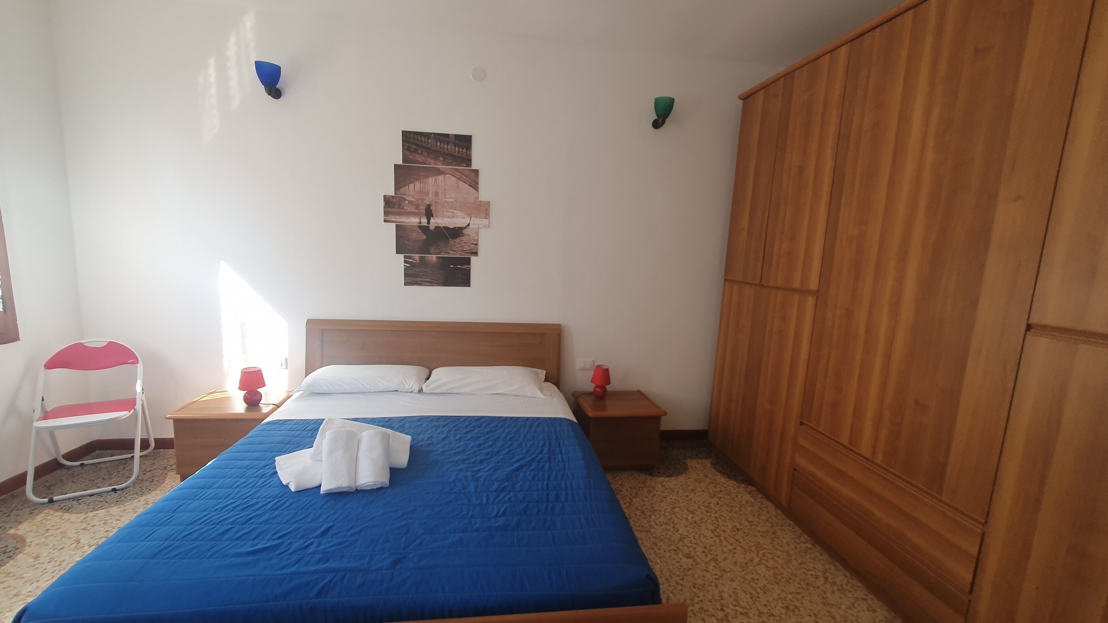 Een slaapkamer met een bed, een houten kledingkast, een stoel en een muur met foto’s.