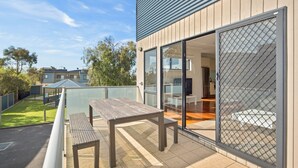 En modern bostadsbyggnad med en balkong, ett träbord och en glasdörr som leder in till ett inre utrymme.
