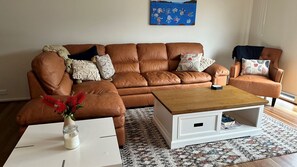 Un sofá de cuero marrón con una mesa de centro de madera y una mesita auxiliar blanca con un jarrón de flores rojas.
