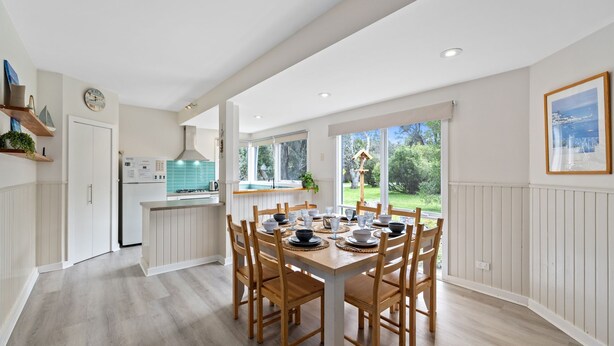 Una cocina moderna con armarios blancos, una isla central y un comedor con sillas de madera y una mesa dispuesta para seis comensales.