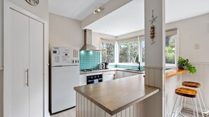 Cocina moderna con refrigerador blanco, estufa a gas y ventana con vistas a la vegetación.