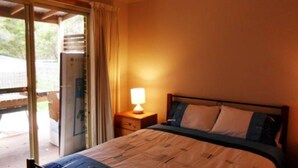 Ein Schlafzimmer mit Bett, Nachttisch mit Lampe und einer Schiebetür zu einem Außenbereich.
