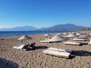 A beach with sun loungers and umbrellas, a clear sky, and mountains in the background. - Stone Built Villa With Private Pool, Gardens And Mountain Views (Dalyan)
