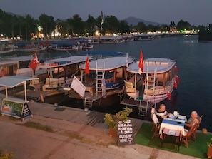 A waterfront restaurant with boats docked in the background, a dining area with tables and chairs, and a sign with a quote.