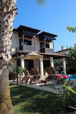 A two-story house with a balcony, a pool, and outdoor seating.