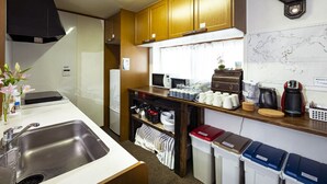A compact kitchen with wooden cabinets, a stainless steel sink, a microwave, and a coffee maker. There is a map on the wall and a trash bin with labeled containers.