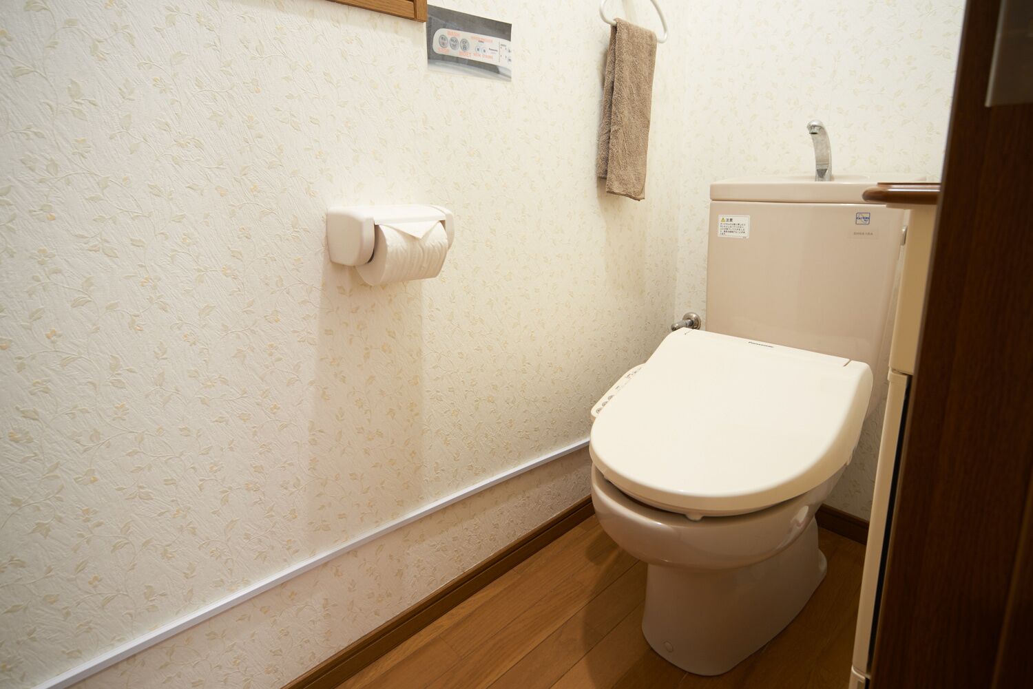 A small bathroom with a toilet, a toilet paper holder, and a towel hanging on a rack.
