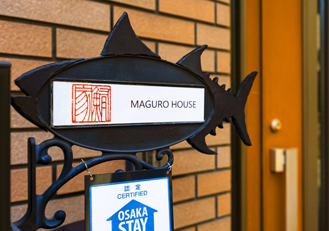 A fish-shaped sign with 'MAGURO HOUSE' and a 'CERTIFIED OSAKA STAY' badge.