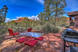 An outdoor patio with a table and chairs, a grill, and a view of red rock formations.