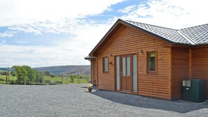 Une cabane en bois avec une allée en gravier, un espace clôturé et une vue sur les collines.