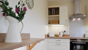 Une cuisine moderne avec un plan de travail en bois, un vase blanc orné de fleurs, une horloge et une hotte de cuisine en acier inoxydable.