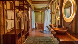 Un baño de madera con una bañera grande de madera, un tocador de madera con un lavabo grande tipo cuenco y un espejo con marco circular.