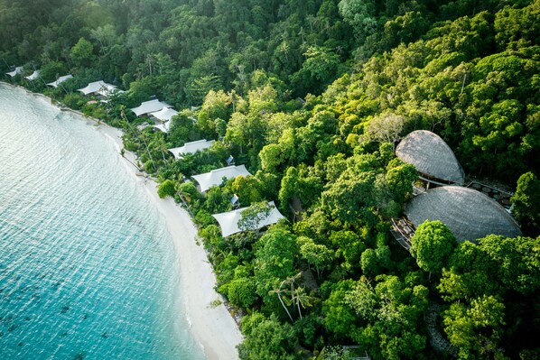 An aerial view of a coastal resort with overwater bungalows, lush greenery, and a clear turquoise sea. - Bawah Reserve (Bawah Island)