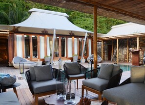 A poolside area with outdoor seating, umbrellas, and a stone wall backdrop. - Bawah Reserve (Bawah Island)