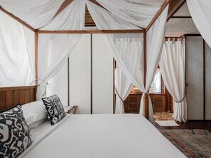 A bedroom with a canopy bed, wooden headboard, and a view of a stone wall and wooden door. - Bawah Reserve (Bawah Island)