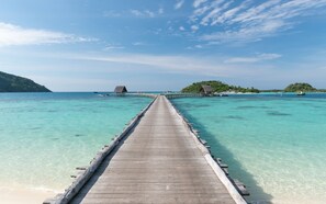 A wooden pier extending into clear turquoise waters, leading to a small island with a thatched-roof hut. - Bawah Reserve (Bawah Island)