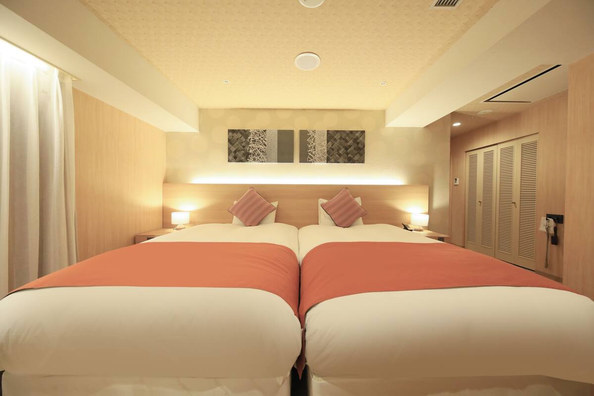 A hotel room with two beds, a headboard with wall art, bedside lamps, and a wardrobe.