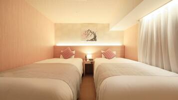 A hotel room with two beds, a nightstand with a lamp, a painting on the wall, and a window with curtains.