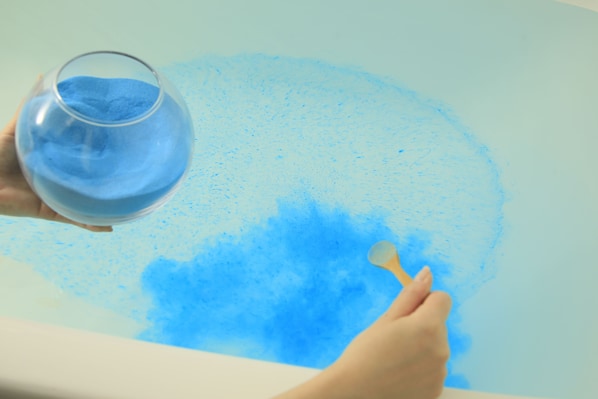 Une main tenant un verre contenant une poudre bleue, qui est versée sur une surface plane.