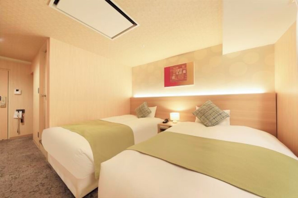 Ein Hotelzimmer mit zwei Betten, einem Nachttisch mit Lampe, einer Tür und einer Wandleuchte.