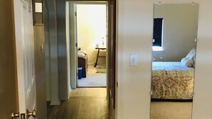 Een gang die leidt naar een slaapkamer met een grote spiegel aan de muur.