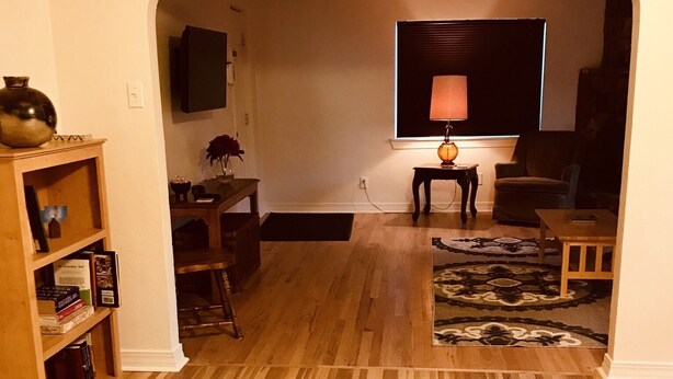 Een woonkamer met een houten vloer, een televisie, een lamp en een boekenkast.