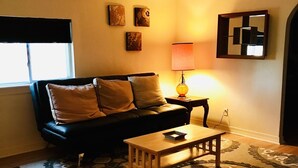 Een woonkamer met een zwarte bank, een houten salontafel, getextureerde vloerkleden en een lamp.