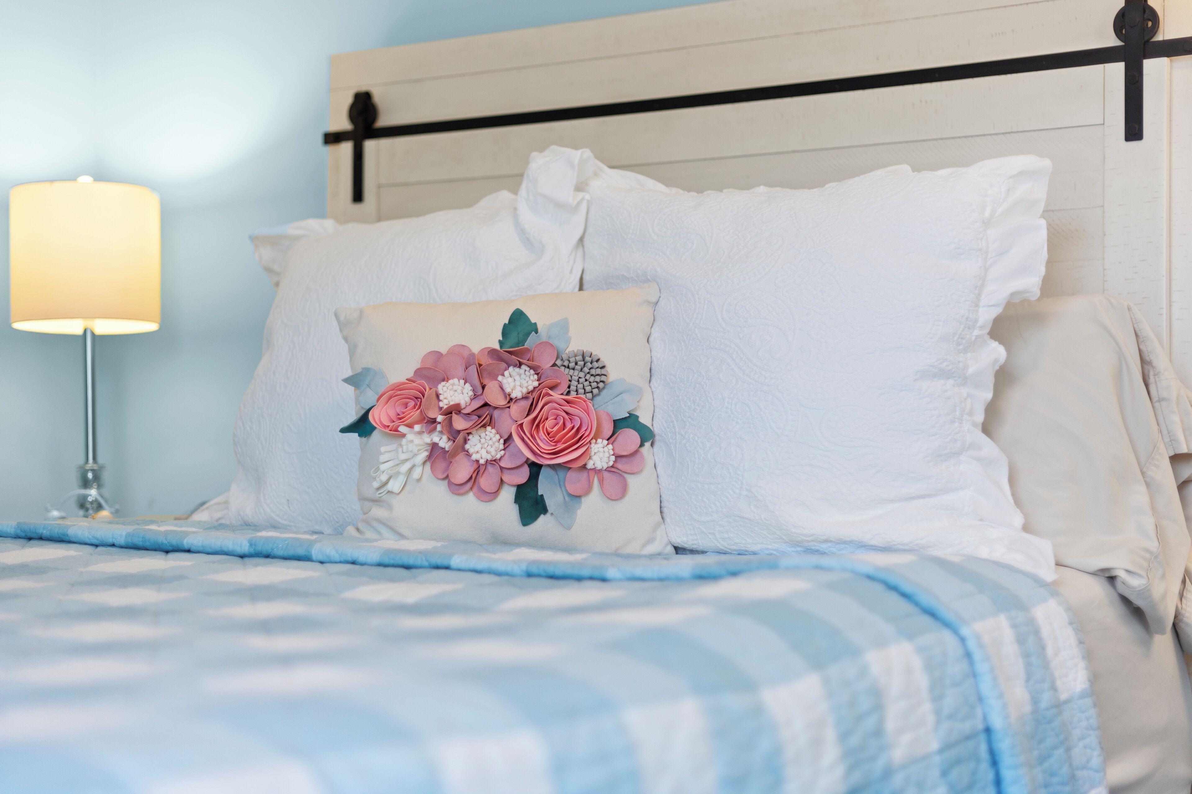 A bed with a blue and white checkered bedspread, white pillows, and a decorative pillow with floral designs.