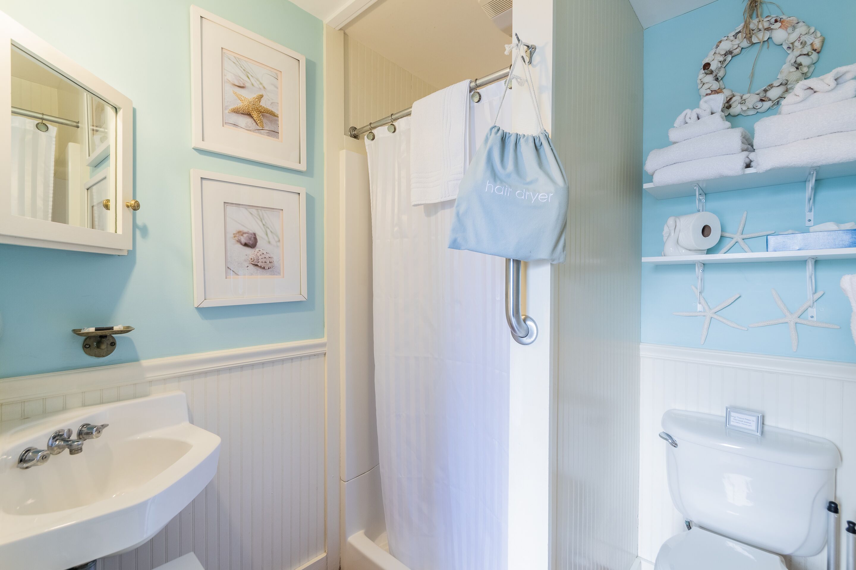 A bathroom with a sink, toilet, and shower curtain. There are framed pictures on the wall and a towel rack with towels.