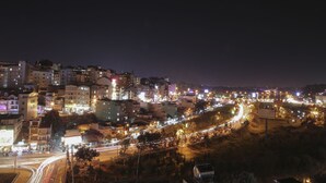 Un paisaje urbano nocturno con edificios iluminados y una carretera sinuosa.