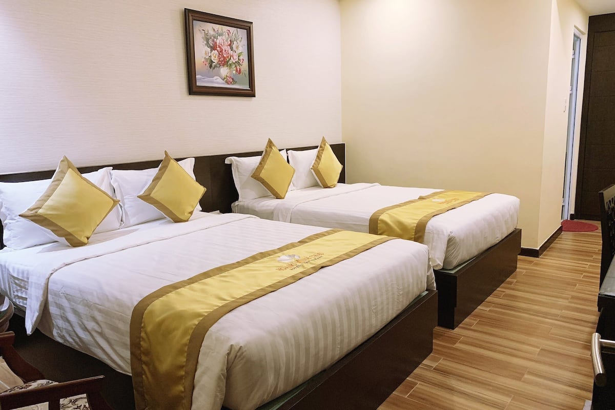 A hotel room with two beds, each with white linens and gold accents, a wooden floor, and a framed floral artwork on the wall.