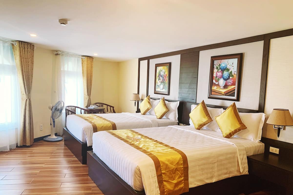 A hotel room with two beds, a fan, a desk, and a chair.