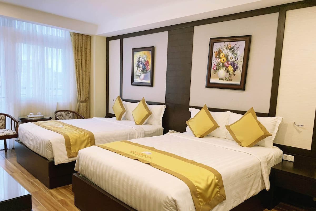 A hotel room with two beds, a small table, chairs, and artwork on the walls.