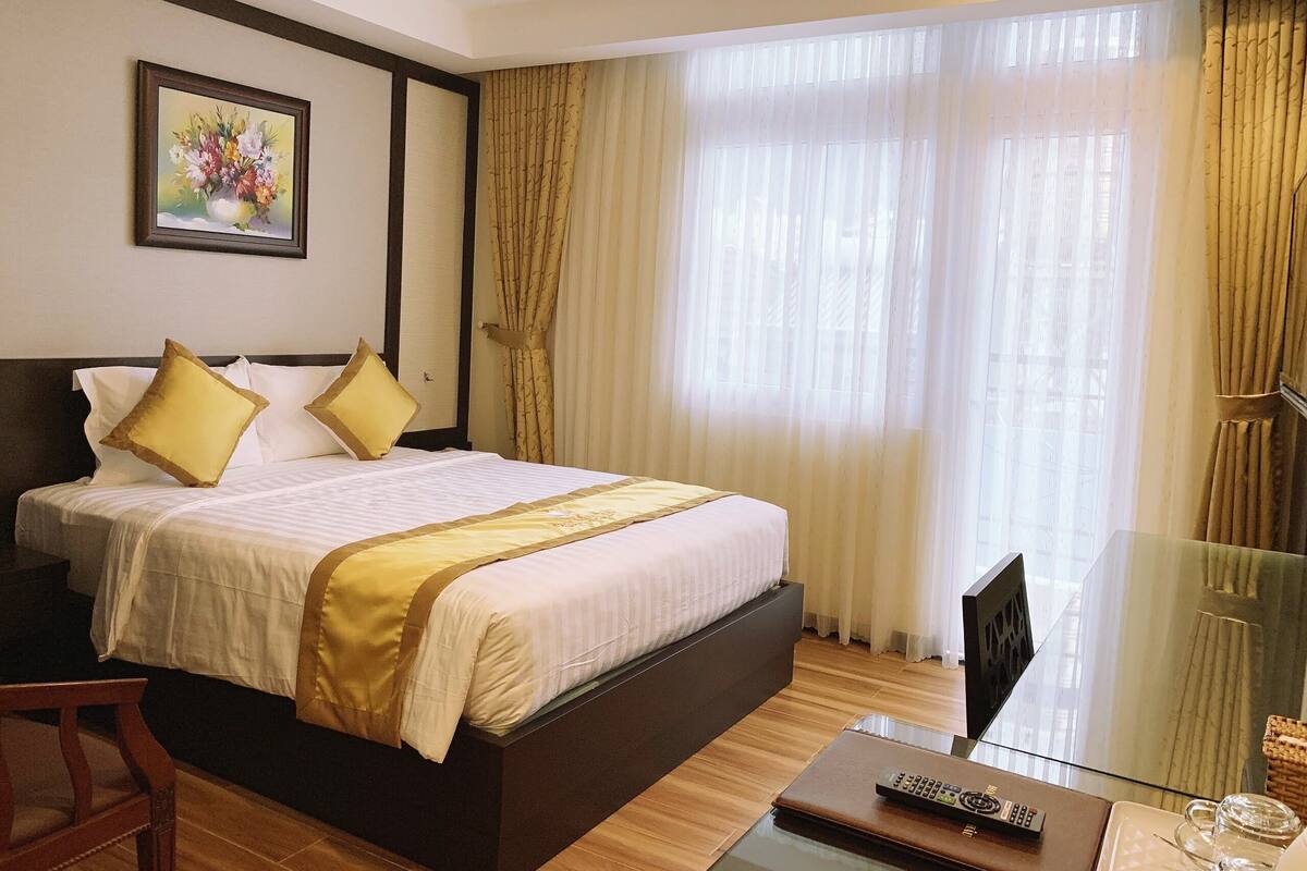 A hotel room with a large bed, a TV, and a glass table with a remote control.