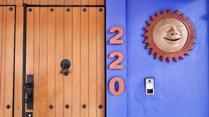 A wooden door with a black handle and a keyhole, a blue wall with the numbers "220" and a sun-shaped decoration, and a doorbell. - Casa Tamayo (Mexico City)