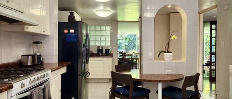 A modern kitchen with white cabinets, a black refrigerator, a stove, and a dining area with two chairs and a small table.