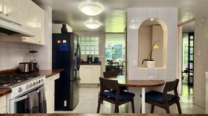 A modern kitchen with white cabinets, a black refrigerator, a stove, and a dining area with two chairs and a small table. - Casa Tamayo (Mexico City)