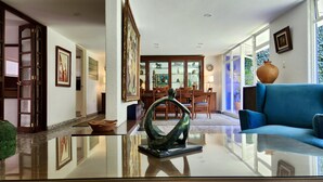 A modern living room with a glass coffee table, a blue sofa, and a dining area with wooden chairs and a glass-top table. - Casa Tamayo (Mexico City)