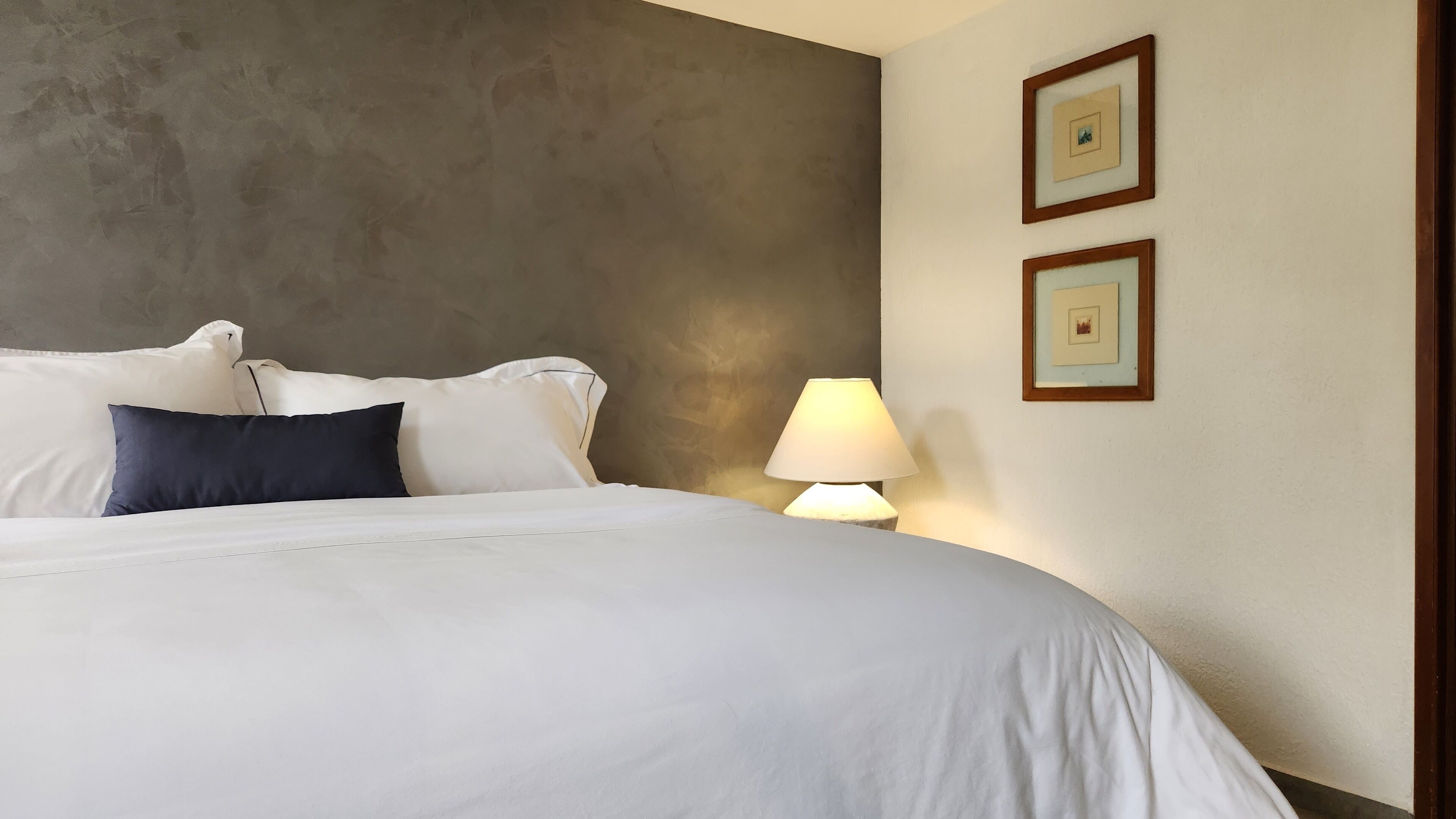 A neatly made bed with white and navy pillows, a bedside lamp, and two framed pictures on the wall.