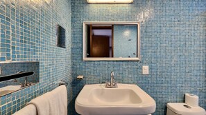 A bathroom with blue mosaic tiles, a white sink, a mirror, and a toilet. - Casa Tamayo (Mexico City)